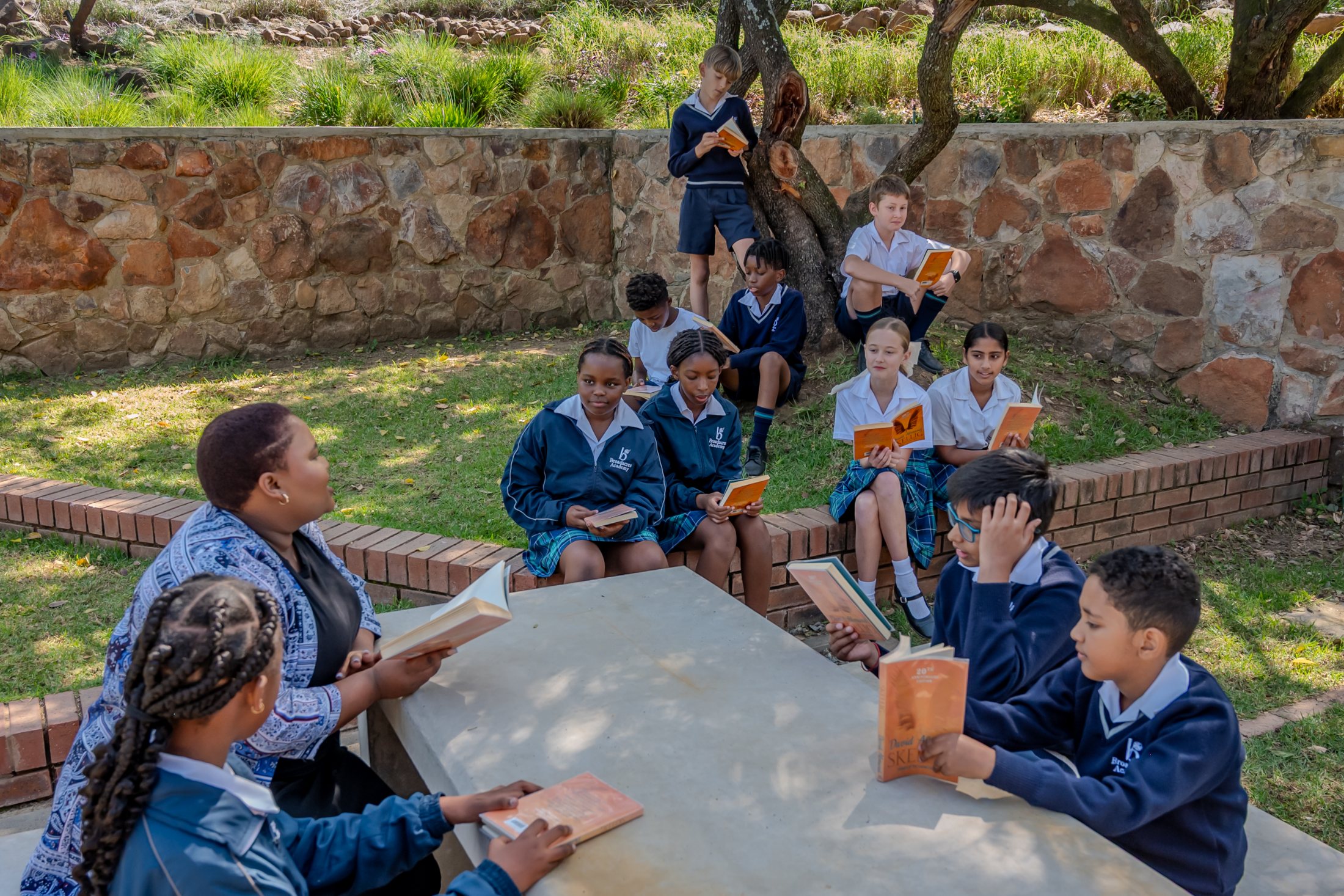 Broadacres pupils reading outdoors with their teacher at a stone bench